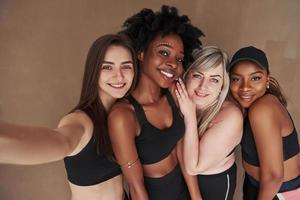 Ya no necesito fotógrafo. grupo de mujeres multiétnicas de pie en el estudio con fondo marrón foto