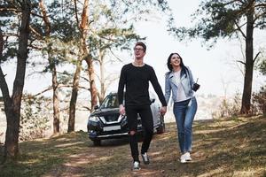 siempre juntos. abrazar y disfrutar de la naturaleza. una pareja ha llegado al bosque en su nuevo auto negro foto