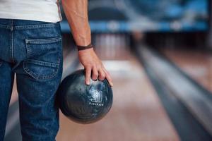 foto enfocada. vista de partículas traseras del hombre con ropa informal jugando a los bolos en el club