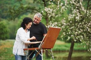 el hombre mira a su esposa. pareja madura tiene días libres y trabaja en la pintura juntos en el parque foto