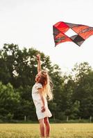Rear view. Happy girl in white clothes have fun with kite in the field. Beautiful nature photo