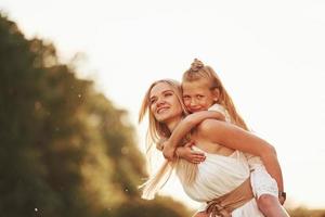 Riding on woman. Mother and daughter enjoying weekend together by walking outdoors in the field. Beautiful nature photo