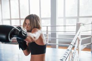 Fast move. Female sportswoman training in the boxing ring. In black colored clothes photo