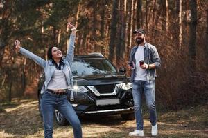 Awesome feelings. Enjoying the nature. Couple have arrived to the forest on their brand new black car photo