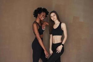Best friends. Two multi ethnic female friends stands in the studio with brown background photo
