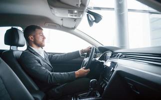 agradable luz del sol. hombre de negocios moderno probando su auto nuevo en el salón del automóvil foto