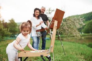 Wooden easel. Grandmother and grandfather have fun outdoors with granddaughter. Painting conception photo
