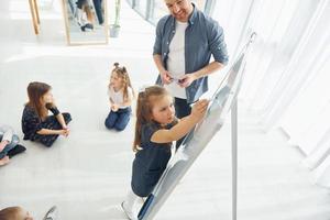 Little girl standing and writing on the board. Group of children students in class at school with teacher photo