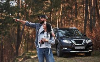 Guy showing something beatiful. Enjoying the nature. Couple have arrived to the forest on their brand new black car photo