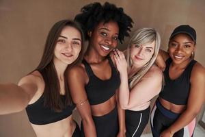 Please smile to the camera. Group of multi ethnic women standing in the studio against brown background photo