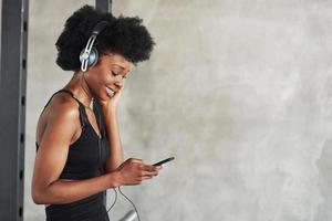 Using smartphone. Portrait of african american girl in fitness clothes having a break after workout photo