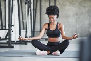 Practicing yoga. African american woman with curly hair and in sportive clothes have fitness day in the gym photo