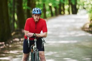 Taking a break. Cyclist on a bike is on the asphalt road in the forest at sunny day photo