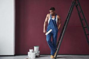 preparándose para la pintura. joven trabajador afroamericano con uniforme azul tiene trabajo que hacer foto