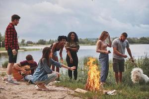 Near the lake. Group of people have picnic on the beach. Friends have fun at weekend time photo