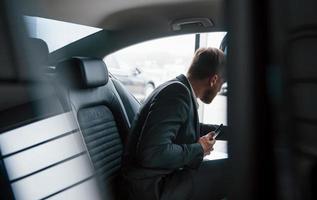 Getting out of the vehicle. Businessman in official wear have call when sitting on the back of car photo