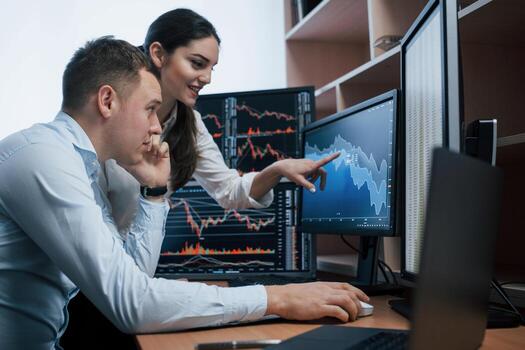 Girl is smiling, guy talks using the phone. Team of stockbrokers are having a conversation in a office with multiple display screens photo