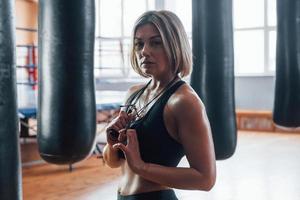 con saltar la cuerda en el cuello. mujer cerca del saco de boxeo negro en el gimnasio. iluminación natural foto