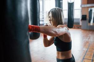 cabello hermoso. la boxeadora está golpeando la bolsa. rubia hacer ejercicio en el gimnasio foto