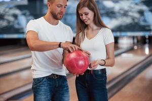 Hold it by that way. Man teaching girl how to holds ball and play bowling in the club photo