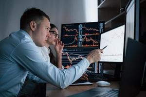 Working at the evening time. Team of stockbrokers are having a conversation in a office with multiple display screens photo