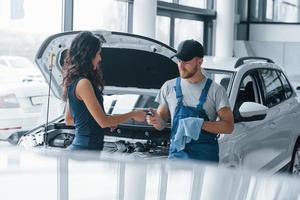 gracias por el trabajo mujer en el salón de autos con un empleado en uniforme azul que lleva su auto reparado de regreso foto