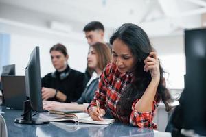 Writing in the notepad. Group of young people in casual clothes working in the modern office photo