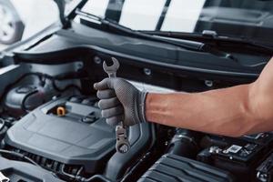 Man's hand in glove holds wrench in front of broken automobile photo