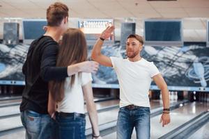 It's awesome game. Young cheerful friends have fun in bowling club at their weekends photo