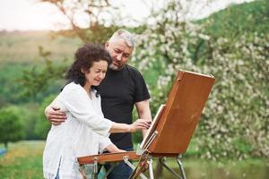 pareja madura tiene días libres y trabaja en la pintura juntos en el parque foto