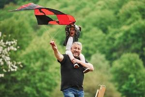 Enjoy the moment. Running with red kite. Child sitting on the man's shoulders. Having fun photo