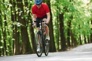 Weekend activities. Cyclist on a bike is on the asphalt road in the forest at sunny day photo