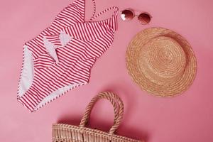 sombrero, anteojos y bolso. bikini en la mesa de color rosa. grupo de objetos para viajar y vacaciones foto