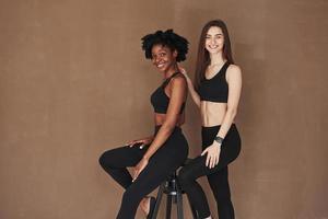 Facial expressions. Two multi ethnic female friends stands in the studio with brown background photo