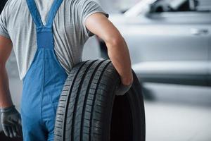 Repair concept. Mechanic holding a tire at the repair garage. Replacement of winter and summer tires photo