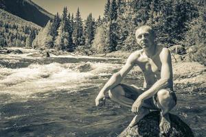 Young man on rock in river Rjukandefossen waterfall Hemsedal Norway. photo