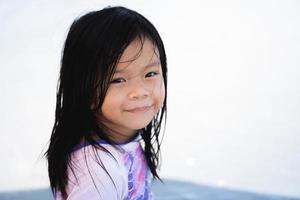 Portrait image child 5 years old. Positive smiling little girl looking at camera. Kid sitting on beach, preschool pretty children with beautiful happy face posing alone at sea, cheerful baby headshot. photo