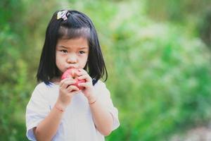 imagen de retrato niño de 4-5 años. la niña asiática está a punto de comer una manzana. A los niños no les gusta comer fruta. espacio vacío para ingresar texto. foto