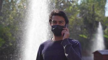 Teenager making a phone call with someone in the park. Close-up phone call. Black surgical mask. pandemic conditions. video