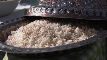 Den Reis in einer großen Pfanne zubereiten. ein Teller Reis und Gemüsestücke. Dampf kommt von einem heißen Mittagessen. Küche zu Hause. Der Reis wird mit einem Holzspatel gemischt. video