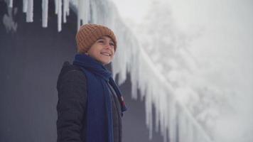 el niño mira a su alrededor riéndose frente a los carámbanos. niño feliz con ropa de invierno en un día de nieve mirando alrededor y riendo. video