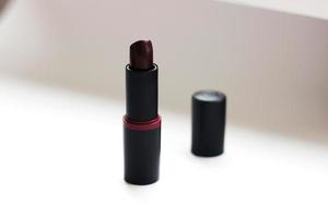 pomada de lápiz labial oscuro abierta de pie sobre fondo claro borroso, foto horizontal. producto cosmético decorativo, belleza y moda, maquillaje. cuidado de la cara de la mujer