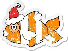 distressed sticker cartoon of a exotic fish wearing santa hat vector