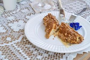 Homemade puff pastry deep fried Eclairs with vanilla cream topping with almonds nut on white plate over table top with lace tablecloth. traditional french dessert. selective focus photo