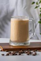 Cold coffee drink glass with ice and cream milk on old white table in abstract silhouette shadow white background of natural leaves tree branch falling on wall. latte and cappuccino refreshment. photo