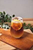 cold iced black brew coffee mixed lemon juice and lemon slices in a glass with pieces of ice on a wooden table, natural light, fresh summer drink in the morning photo