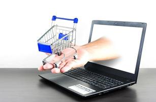 shopping cart in hand with Computer notebook blank screen on wood table photo