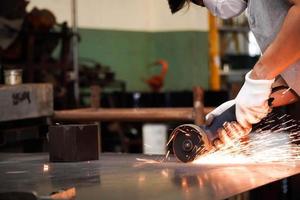 mechanic works with an electric steel grinder in the factory. sparks from the grinding wheel photo