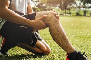 los hombres heridos por el ejercicio usan las manos para sostener las rodillas sobre la hierba verde foto