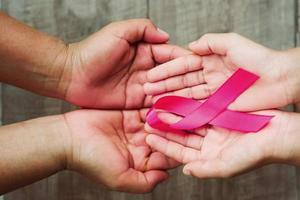 concepto de salud y medicina. mano que sostiene la cinta rosa en la madera. conciencia del cáncer de mama. señal de esperanza foto